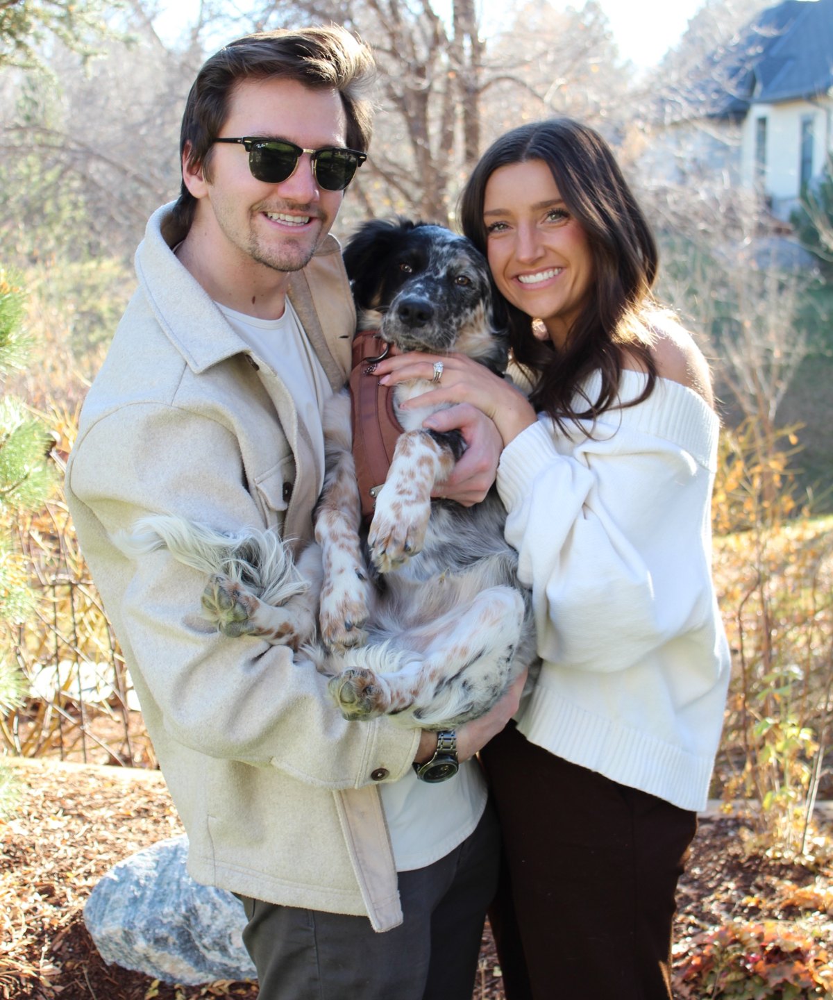 Peyton and Kylie Manning holding their dog Bauer outside on a sunny fall day